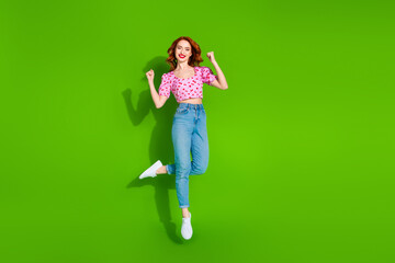 Photo of lucky positive woman wear print top jumping high rising fists empty space isolated green color background