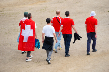 Swiss fans in red outfits, proudly displaying national symbols and flags with white crosses,...