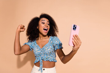 Photo of charming lucky woman wear blue top winnin game modern device empty space isolated beige...
