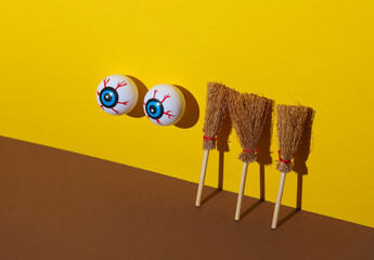 Eyeballs with brooms on yellow brown background. Minimalistic Halloween still life. Creative layout