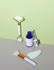 Serum bottle, jade massage roller and gua sha scraper on green gray background. Skin care