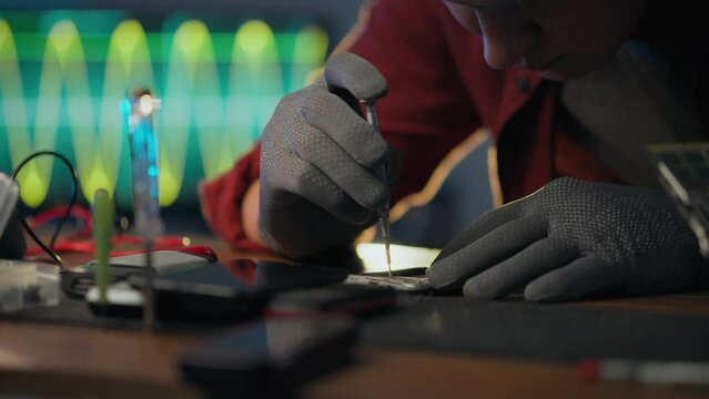 To correct. An electronic technician wearing protective gloves focuses on using a screwdriver in an electronics workshop. Electronics service technician unscrews screws performs service, work