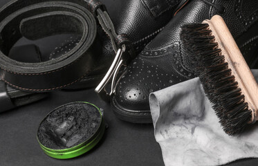Leather boots, belt and wallet with wax, rag and brush on black background. Leather care