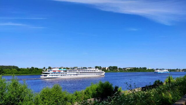 River cruise ship on Volga river seen from the embankment of a small town. Passenger boat sailing on a summer day against the picturesque landscape of woods