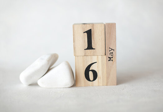 Wooden block calendar with date May 16 on a concrete background with pebbles