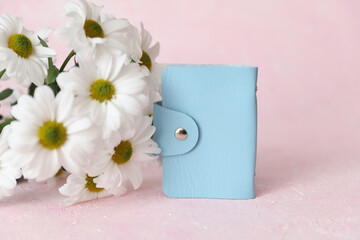 Blue leather wallet business card holder and flowers on pink concrete background