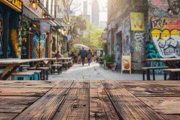 Fototapeta premium A wooden table in the foreground with a blurred background of an urban street cafe. The background features outdoor seating, pedestrians walking by, street art on nearby buildings.