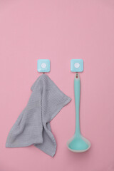 Ladle and towel hang on hooks. Kitchen tools. Pink background