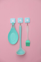 Kitchen utensils hang on hooks. Pink background
