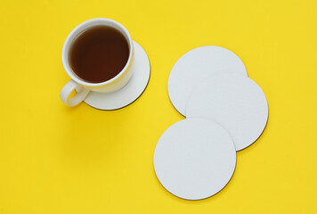 Mockup of white empty coasters and coffee cup on a yellow background