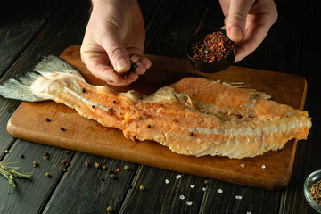 Cooking salmon fish on the kitchen table. A chef adds spices to a fish steak with his hands before baking in the oven