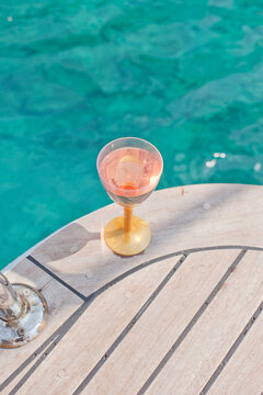 Pink wine in a glass on a yacht against the background of the azure sea.