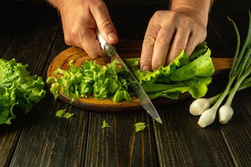 A chef uses a knife to cut lettuce leaves on a wooden board before preparing a vegetarian meal. Advertising space