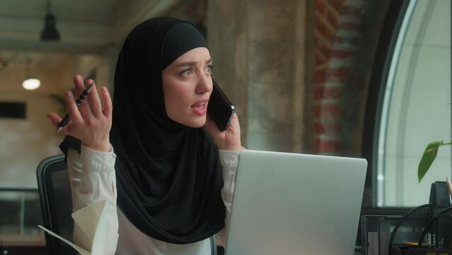 Muslim angry annoyed woman hijab islamic Arabian business lady girl female businesswoman mad furious boss talking mobile phone multitasking search data laptop solve problem conflict quarrel in office