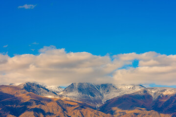 white clouds above snowcapped mountains at autumn afternoon