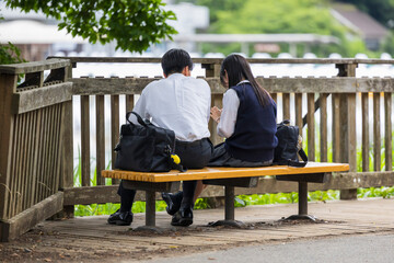 公園のベンチに座る仲良し高校生男女