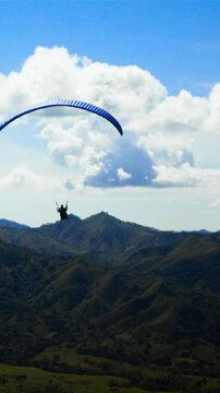 4k ultra hd. Two People ride gliding Paramotor paraglide paraplane fly in the sky with mountains midday sunny. Blue clouds. Vertical shot.