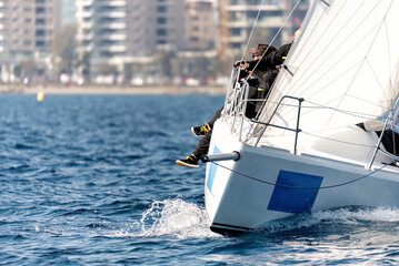 Sailors maneuvering a sailboat during a competitive regatta near the city coastline