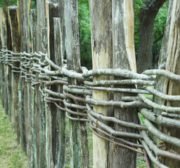 Fototapeta premium Wooden fence assembled of beams or logs old patched up woven wicker with bits of wood. Natural building concept. Green background nature 