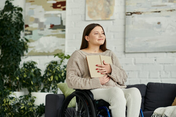 A young woman sits in a wheelchair in her living room, holding a book close to her chest.