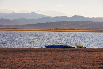 old pedal catamarans and boat on beach of mountain lake at sunny autumnal afternoon.