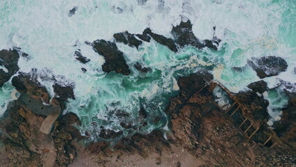 Top sea water foaming on rugged coastal rocks. Turbulent ocean waves bubbling