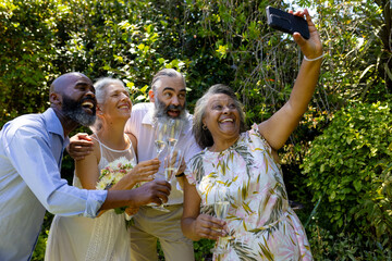 Celebrating with champagne, diverse group of senior friends taking selfie outdoors