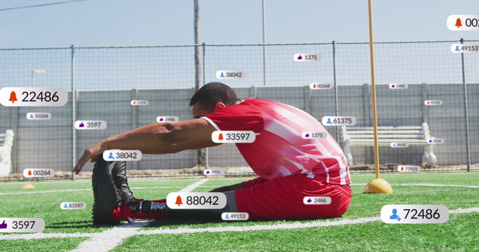 Image of multiple notification bars over biracial soccer player doing stretching on ground - Powered by Adobe