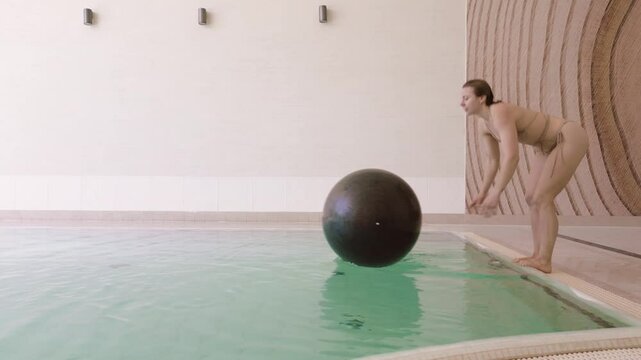 Caucasian woman leaps and fails to land on floating exercise ball in pool, slomo