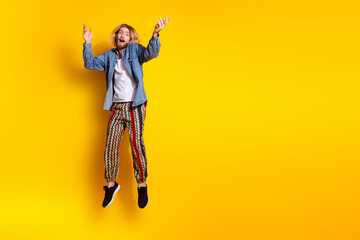 Full size photo of pretty young guy jumping excited wear trendy jeans outfit isolated on yellow color background