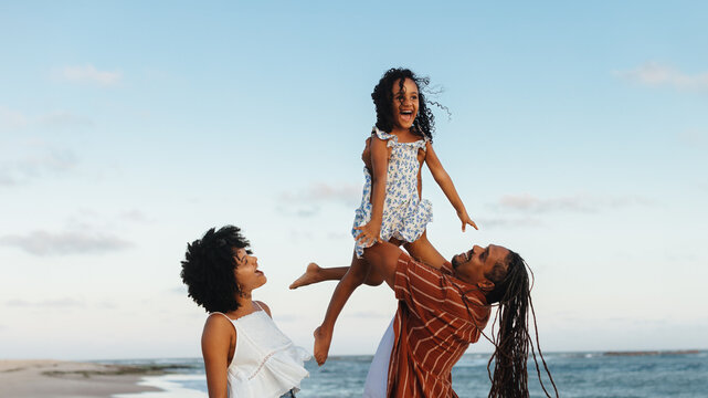 Happy family enjoying a beach vacation with parents lifting child in the air - Powered by Adobe