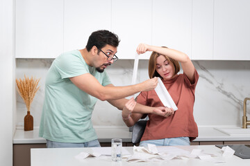 Family financial crisis concept. Shocked and stressed couple counting expenses, taxes and debts. Laptop and many bills on the table