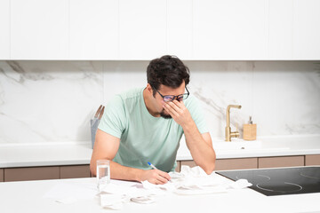 Close up of unhappy man sitting at the table, stressed and confused by calculate expense from...