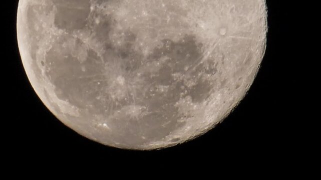 View of a full moon as it moves slowly a little upwards, showing the craters and other landforms that can be seen on the moon's face.