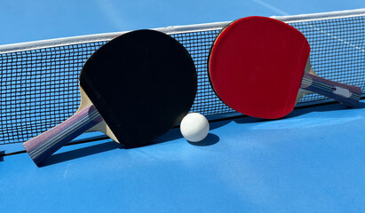 Two table tennis rackets and balls on a blue table with net.