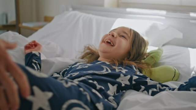 Mom tickling overjoyed toddler at bed closeup. Laughing little girl having fun
