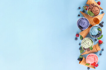 Colorful bright ice cream on bowls, with waffle cones and berries, on light blue background. Variety of ice cream with different flavor with fresh berries top view copy space layout background