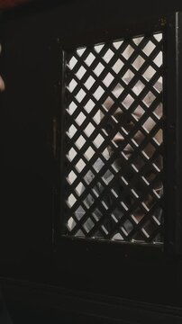 Vertical shot of senior Caucasian priest sitting in confessional and having conversation through lattice screen with Black penitent