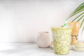 Cold green matcha latte drink.  Delicious iced matcha green tea mixed with ice cubes and whipped creamy milk in latte glass on white table background