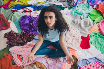 High angle view full size photo of young girl sitting think pile stack clutter clothes apartment...