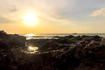 The setting sun casts a golden glow over the rocky beach.