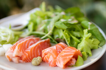 A plate of delicious-looking salmon sashimi. The salmon is served on a bed of lettuce and garnished with wasabi and pickled ginger.