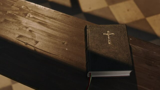 Top down close-up shot of Bible with cross on wooden pew in church