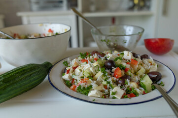 Fresh prepared homemade greek rice salad with feta cheese, peppers, cucumber, apples and black olives on a plate ready to eat on kitchen counter