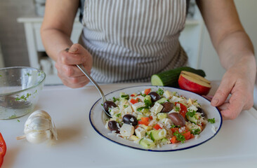 Woman preparing a healthy salad with rice, vegetables and feta cheese in the kitchen