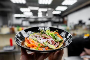 Vibrant dish with meat, greens, and garnishes against a blurred kitchen background