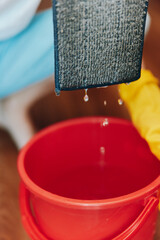 Person in rubber gloves holding bucket of water over red bucket with cloth on top