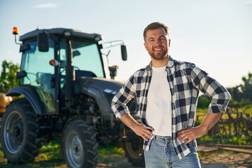 Standing near tractor. Adult farmer is outdoors