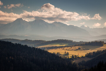 Fototapeta premium A beautiful autumn landscape of the Tatra Mountains seen from Polish Podhale during the golden hour. The sky is painted in warm hues, with the mountains bathed in golden light.