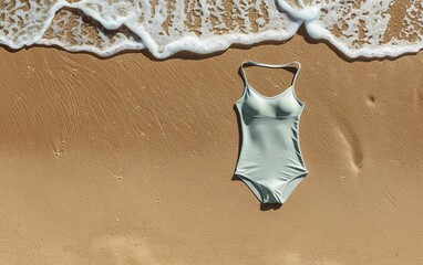One-piece swimsuit lying on sandy beach with gentle waves. Ideal for summer, vacation, poolside, and beachwear imagery.